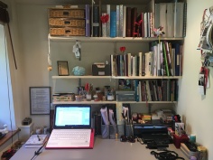 A tidy desk with a laptop on it and shelves with notebooks above
